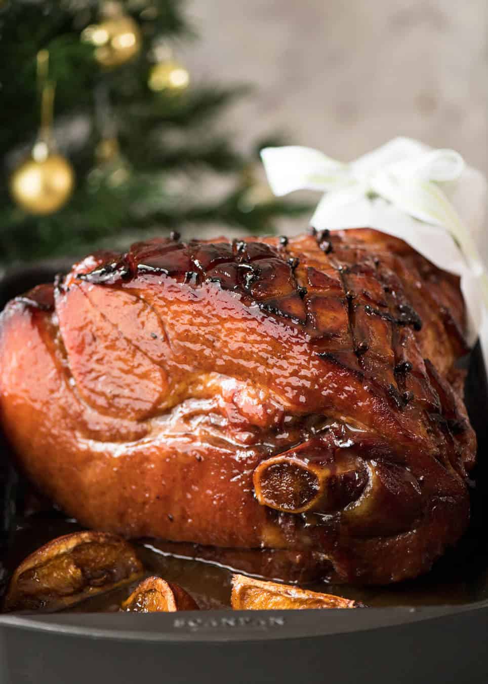 A baked ham glistening with a maple brown sugar glaze on a large white platter.