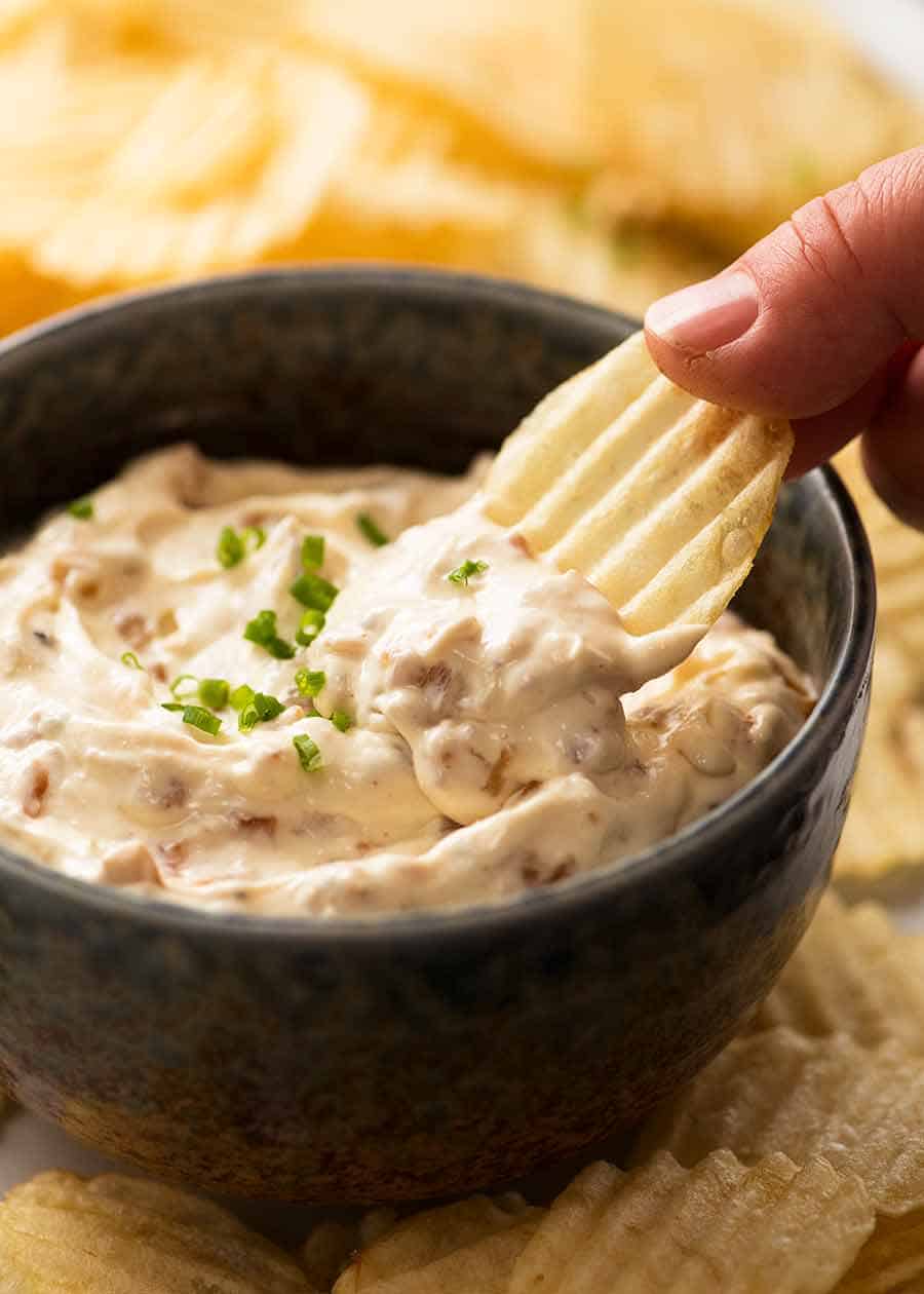 Hand dipping crinkle cut potato chips in creamy homemade French Onion Dip