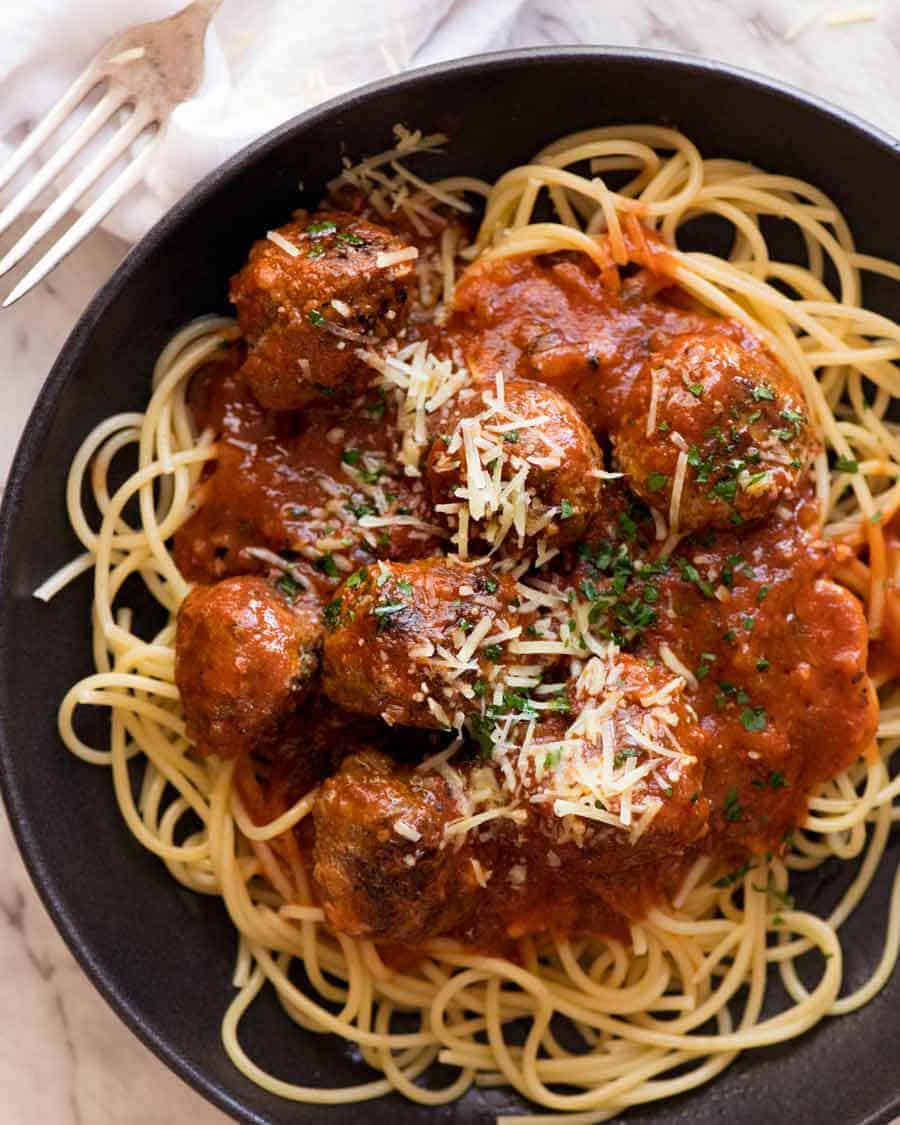 Overhead photo of Italian Meatballs in a rustic black bowl garnished with parmesan, ready to be eaten
