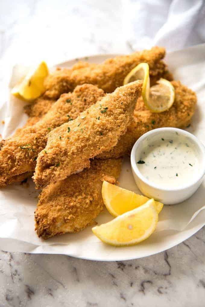 A pile of Oven Fried Chicken Tenders with lemon wedges and ranch dipping sauce on the side.