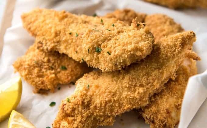 A pile of Oven Fried Chicken Tenders with lemon wedges.