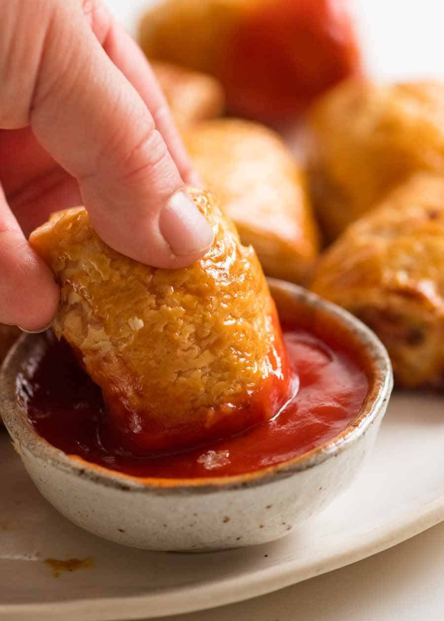 Close up of hand dipping Sausage Rolls in tomato sauce
