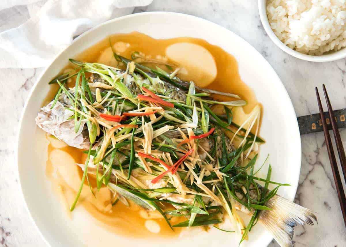 A Chinese Steamed Fish topped with Ginger and Shallots and seasonings, with hot oil poured over it to create a dramatic sizzle and an amazing sauce. So simple, yet so utterly delicious. Steam OR bake the fish! www.recipetineats.com