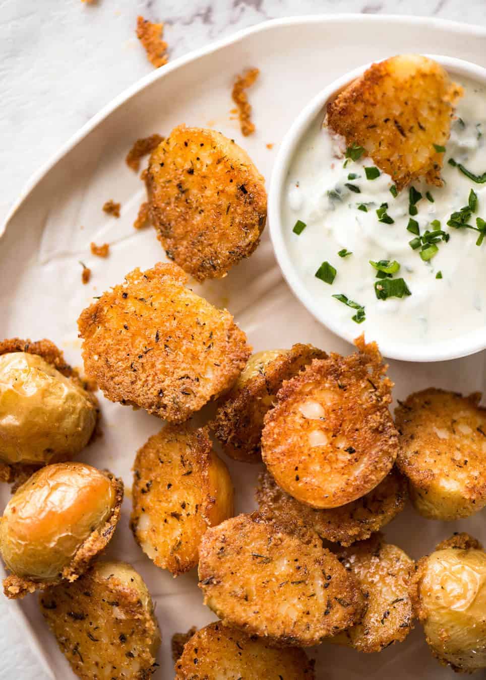 Overhead photo of crispy Parmesan Crusted Potatoes on a rustic white plate with a small bowl of sour cream for dipping.