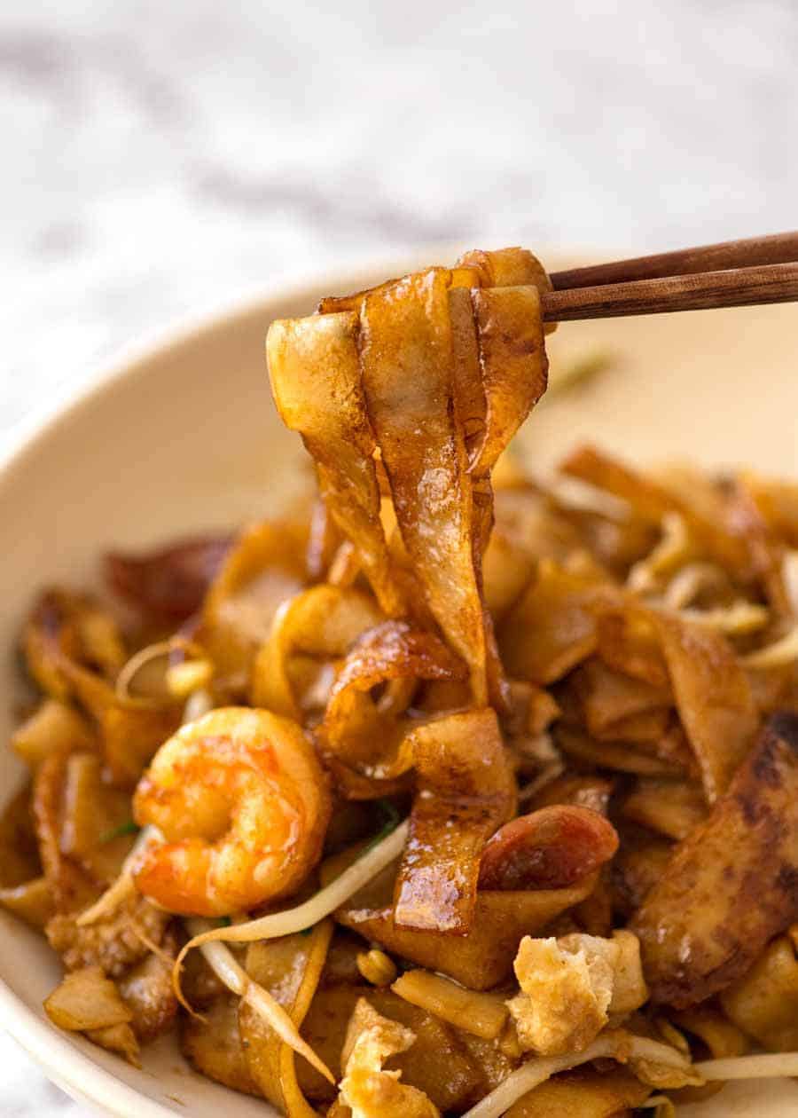 Close up of chopsticks pulling Char Kway Teow noodles out of a bowl