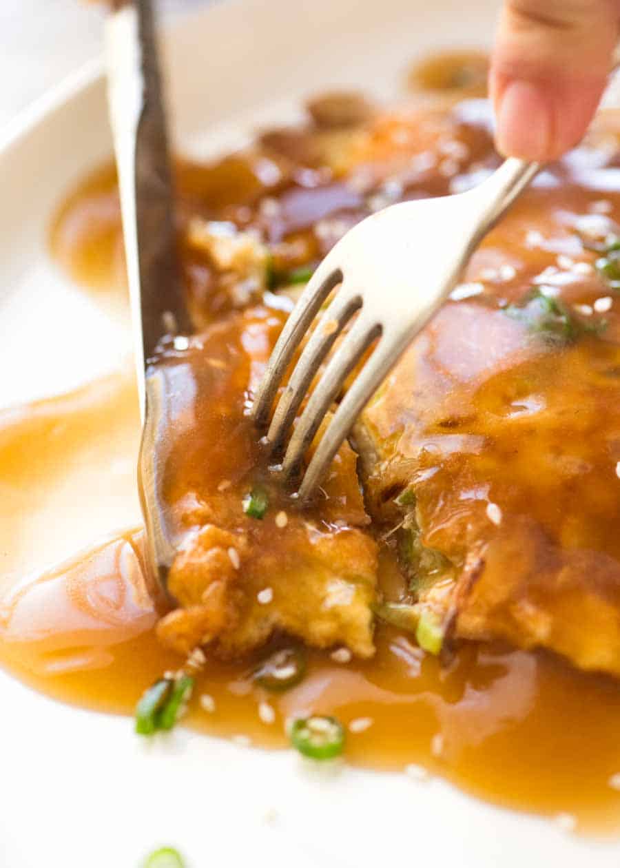 Close up of knife and fork cutting into an Egg Foo Young (Chinese Omelette) smothered in Egg Foo Young Sauce