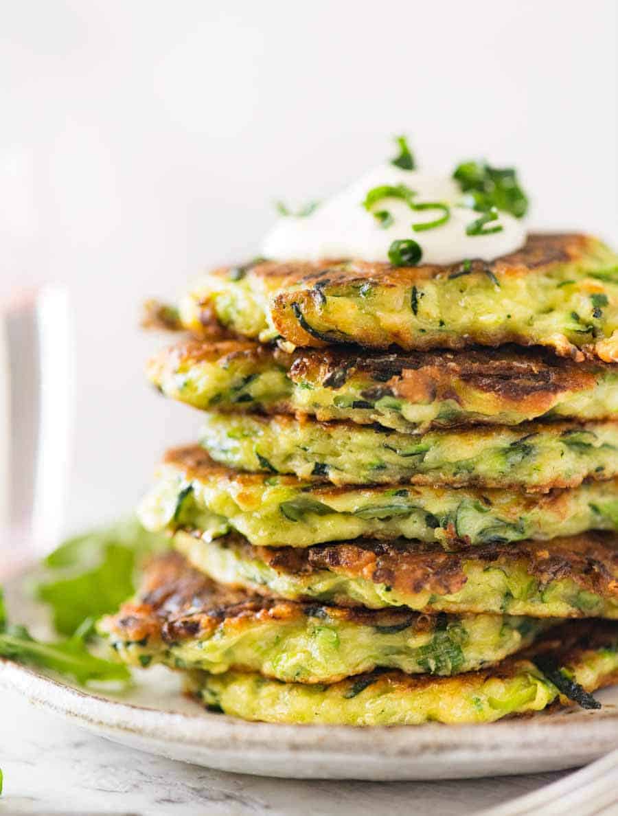 Stack of Crispy Zucchini Fritters with a dollop of sour cream on a rustic brown plate with a side of arugula salad,