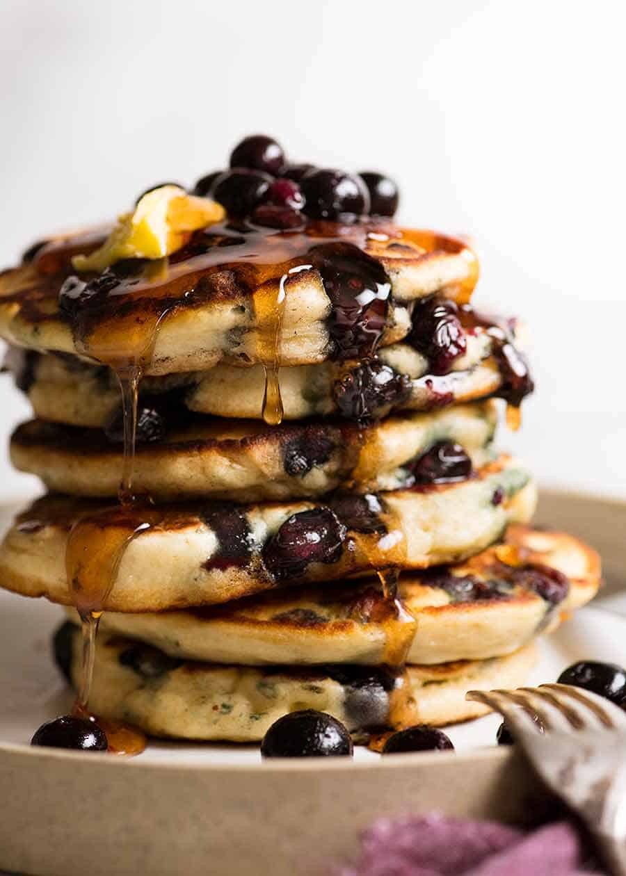 Stack of Fluffy Blueberry Pancakes dripping with maple syrup and melted butter