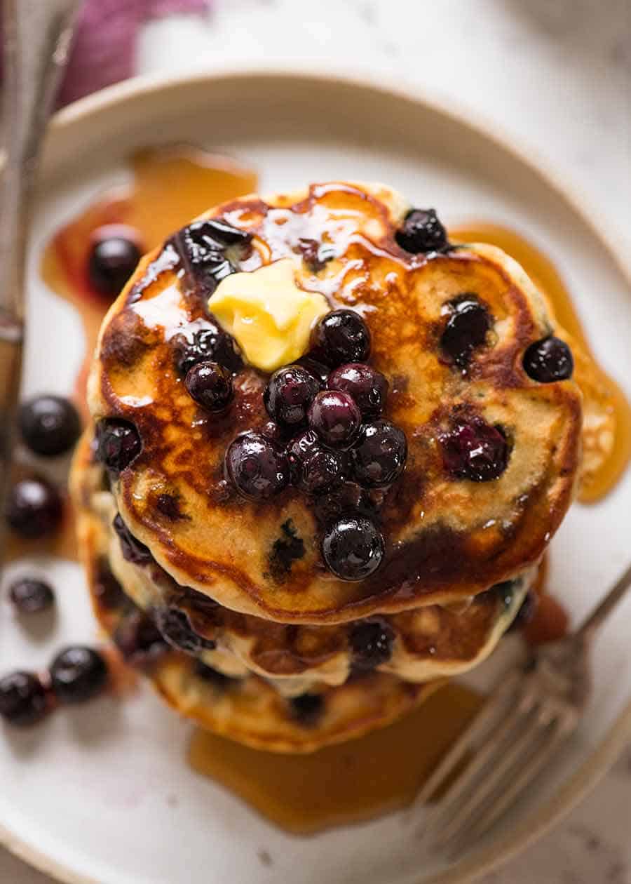 Overhead photo of a stack of Fluffy Blueberry Pancakes with maple syrup and butter