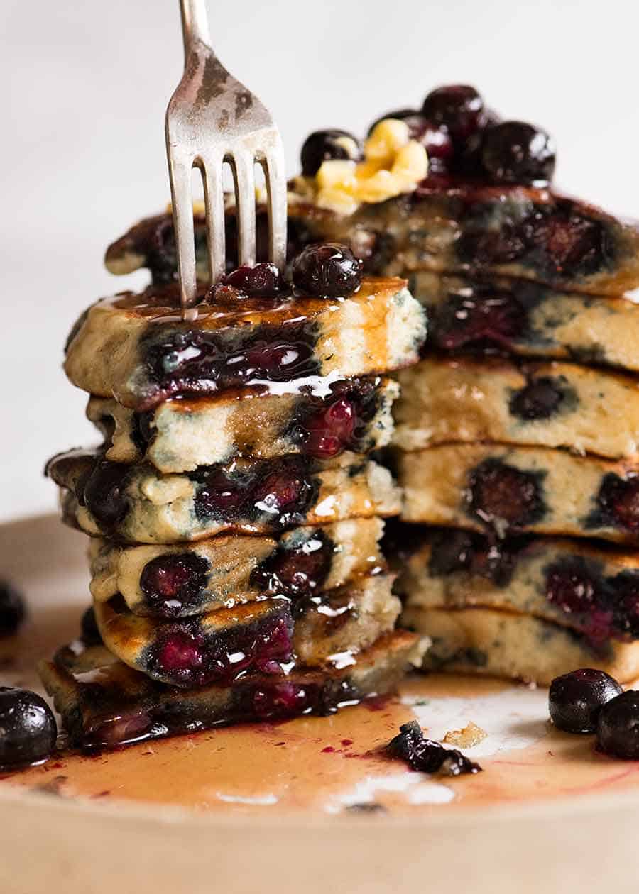 Stack of Fluffy Blueberry Pancakes cut to show how fluffy it is inside, dripping with maple syrup and melted butter
