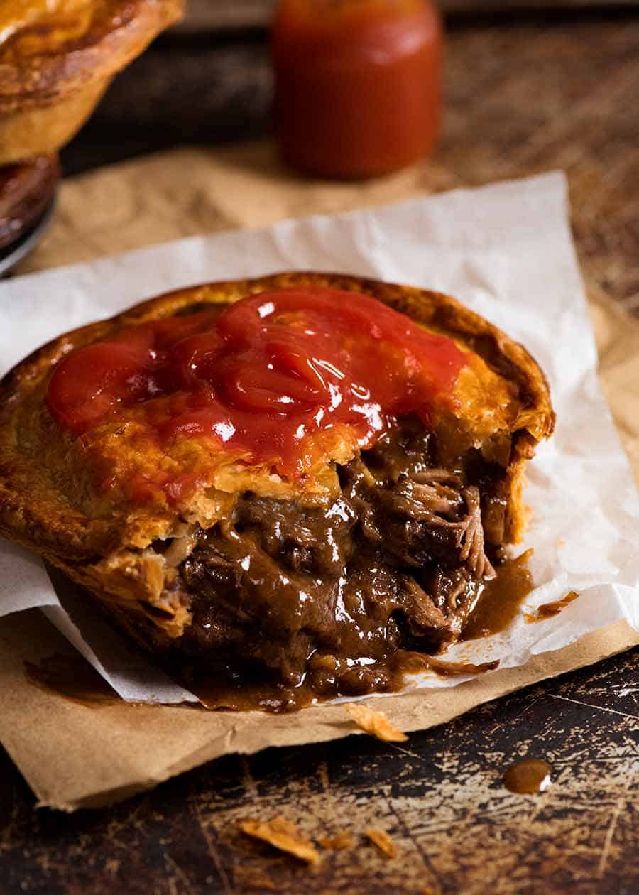 Close up of Meat Pie cut open to show meat pie filling inside, with tomato sauce on top