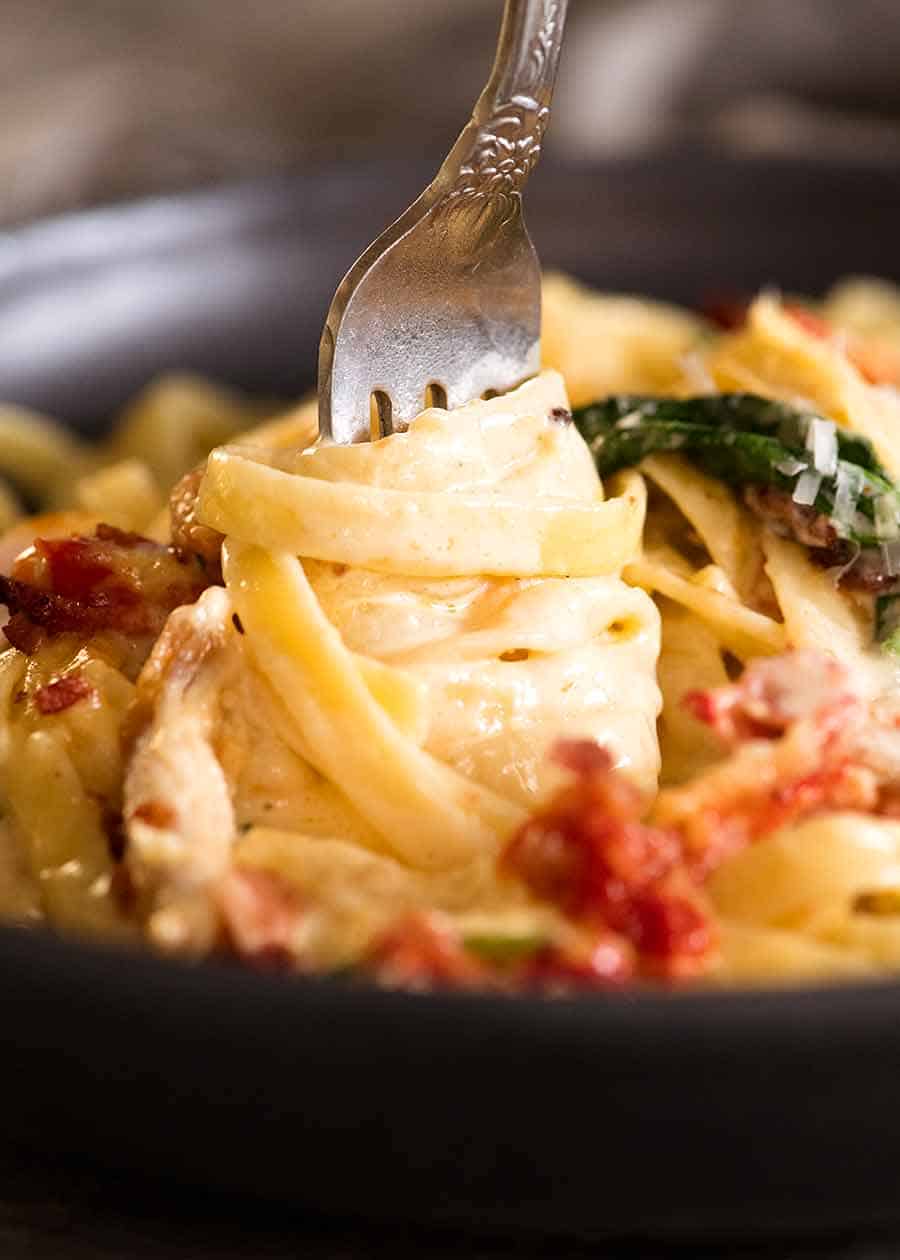 Close up of fork twirling creamy chicken pasta with sun dried tomato, spinach and bacon