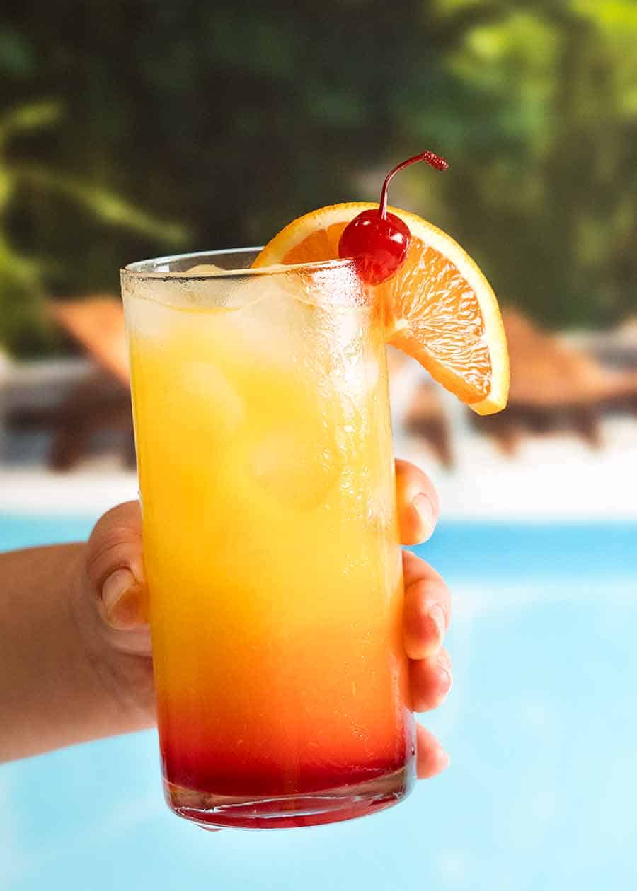 Hand holding Tequila Sunrise by a pool