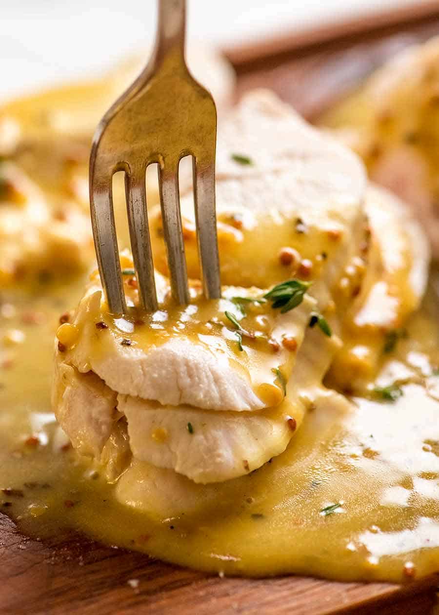 Close up of fork stabbing piece of Poached Chicken breast with Honey Mustard Sauce